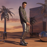 Model wearing an AR vintage black hoodie and silver pants standing in a futuristic desert landscape with metallic palm trees and a reflective building.
