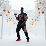 male model wearing a black t-shirt with graphics and QR code for AR video activation, standing in an all-white studio landscape with orange trees while holding a negroni.