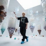 male model standing in a room filled with large futuristic bubble tea, wearing a black t-shirt with QR code for AR video activation.
