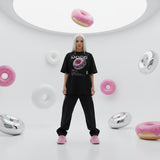 Blonde model wearing a black t-shirt with a donut graphic in a futuristic setting with floating donuts and circular structures.
