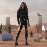 Woman in futuristic outfit and a black hoodie with QR code for AR video activation, standing in a desert landscape with alien structures.